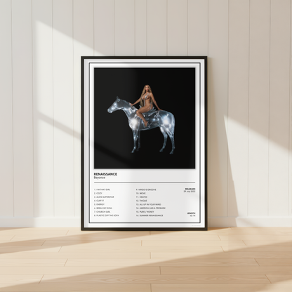 A framed music poster for 'Renaissance' by Beyonce, leaning against a white paneled wall on a light wood floor. The poster features a black background with a central graphic of a woman riding a metallic horse, and a tracklist printed below on a white section.