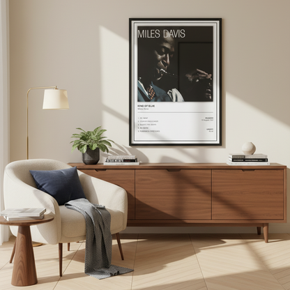 A framed Miles Davis 'Kind of Blue' music poster leaning against a white paneled wall on a light wood floor, with soft sunlight casting shadows across the scene.