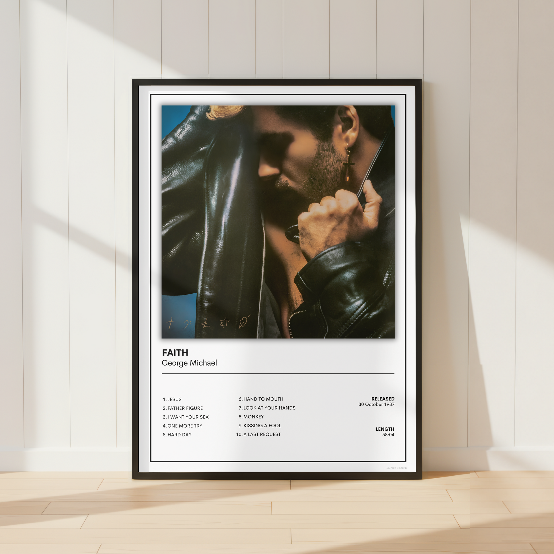 A framed music poster of George Michael's song 'Faith' leaning against a white paneled wall on a light wood floor, with soft sunlight casting shadows.