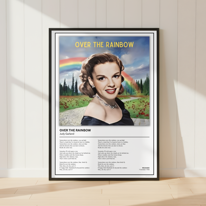 A framed poster titled 'OVER THE RAINBOW' leaning against a white paneled wall on a light wood floor. The poster features a vintage-style portrait of a woman with a rainbow and landscape in the background, plus song lyrics printed below.