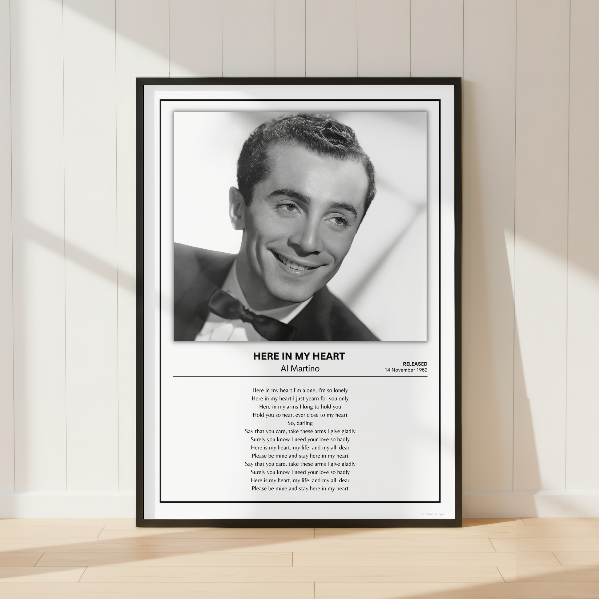 A framed black-and-white portrait print of Al Martino leaning against a light beige paneled wall on a pale wood floor. The print includes a black frame, white mat, the portrait, and printed text below reading 'HERE IN MY HEART' with 'Al Pacino' and 'Marilyn' visible.