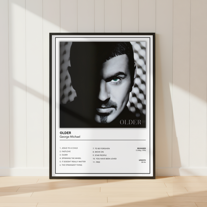 A framed black and white music poster of George Michael's album 'Older' leaning against a white paneled wall on a light wood floor, with soft sunlight casting shadows.