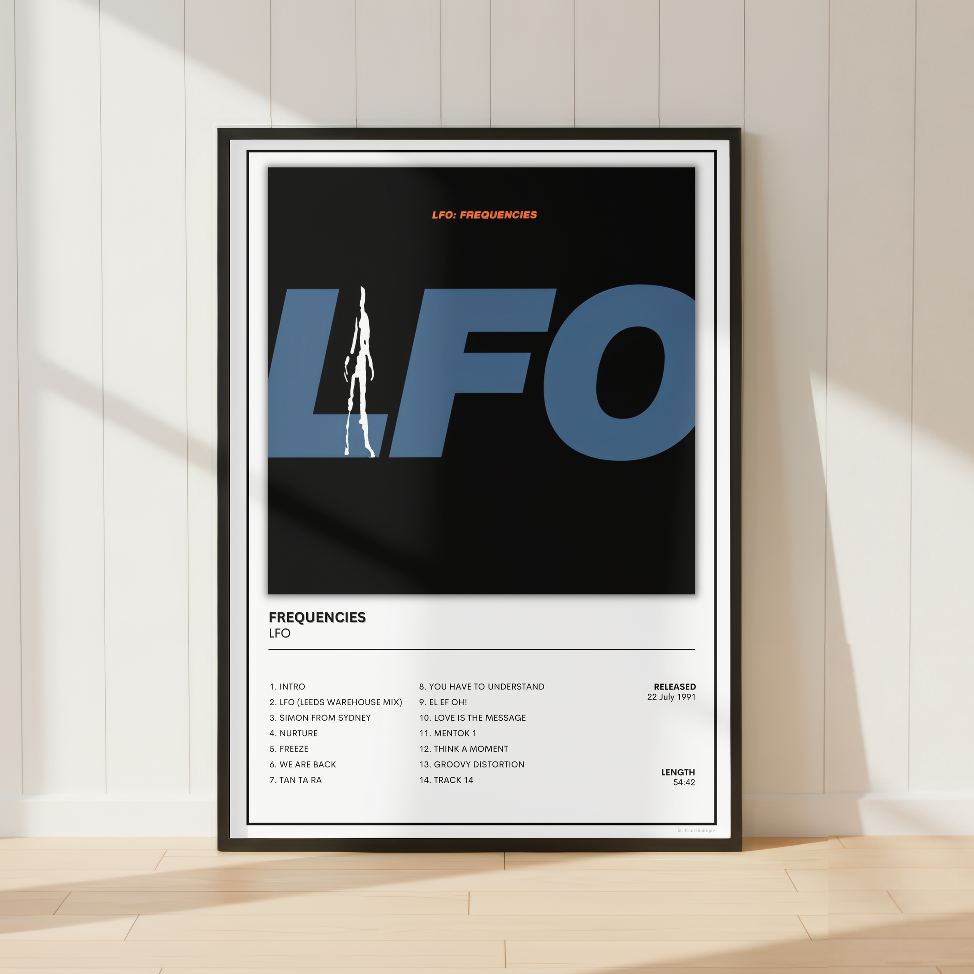 A framed music poster for the band LFO, featuring a minimalist black and blue graphic with tracklist details below, leaning against a white paneled wall on a light wood floor.