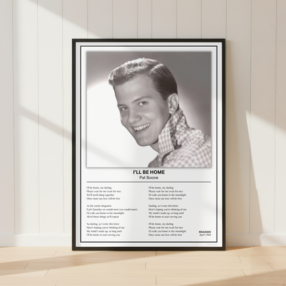 A framed black-and-white Pat Boone 'I'll Be Home' song poster is displayed leaning against a white paneled wall on a light wood floor, with soft window shadows cast across the scene.