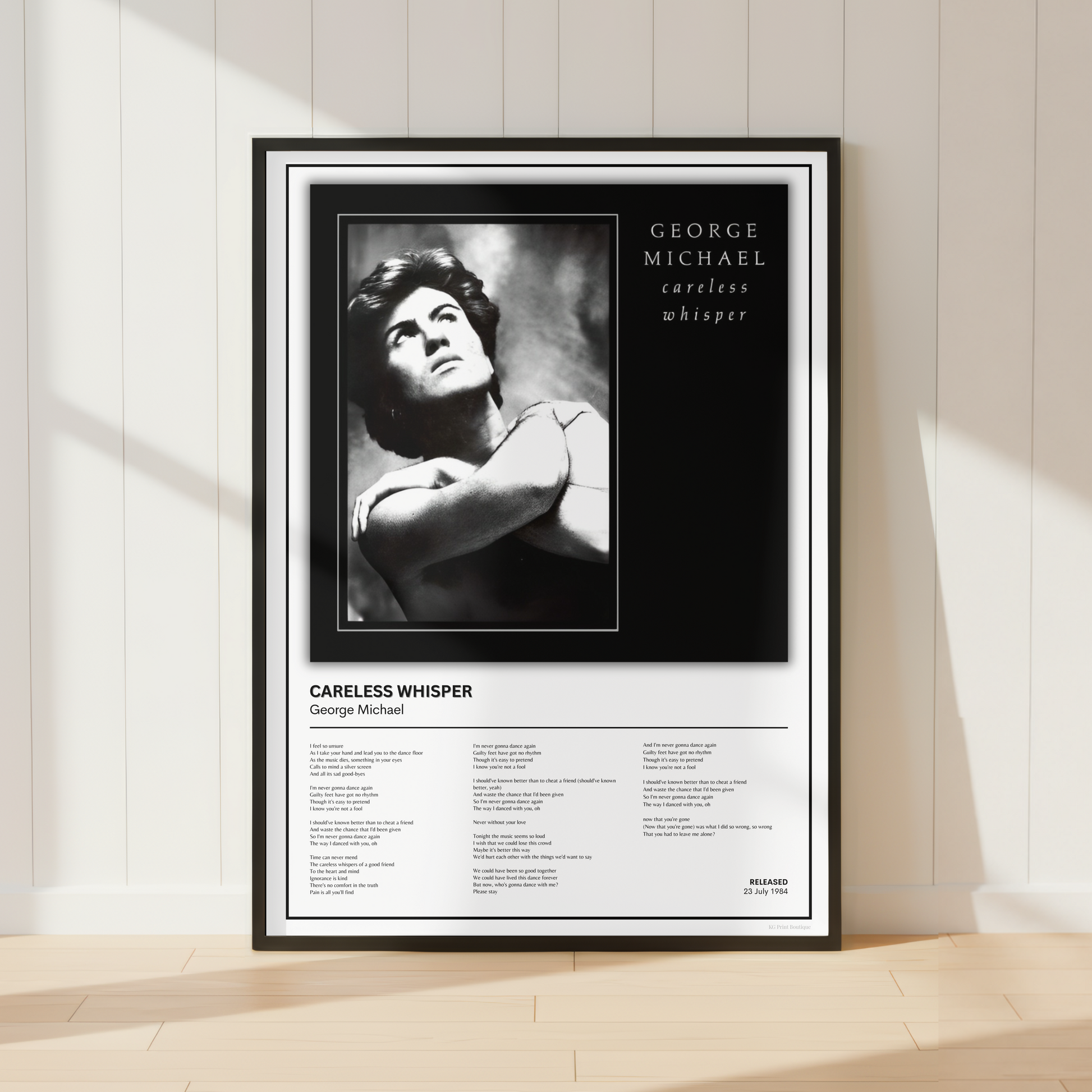 A framed black-and-white music poster for George Michael's album 'Careless Whisper' leaning against a white paneled wall on a light wood floor.