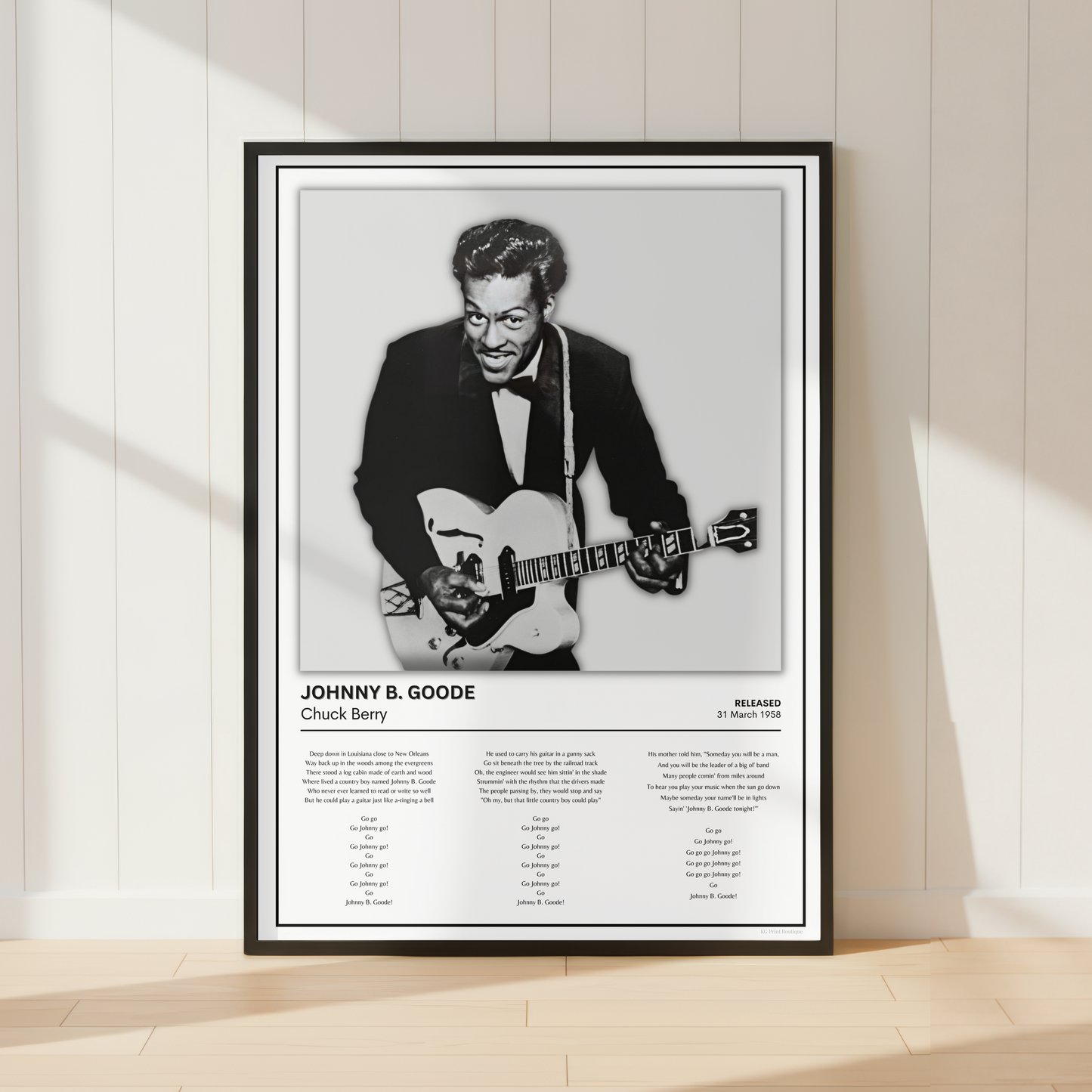 A framed black-and-white poster of jazz musician Johnny B. Goode leaning against a white paneled wall on a light wood floor, with soft window shadows cast across the scene.