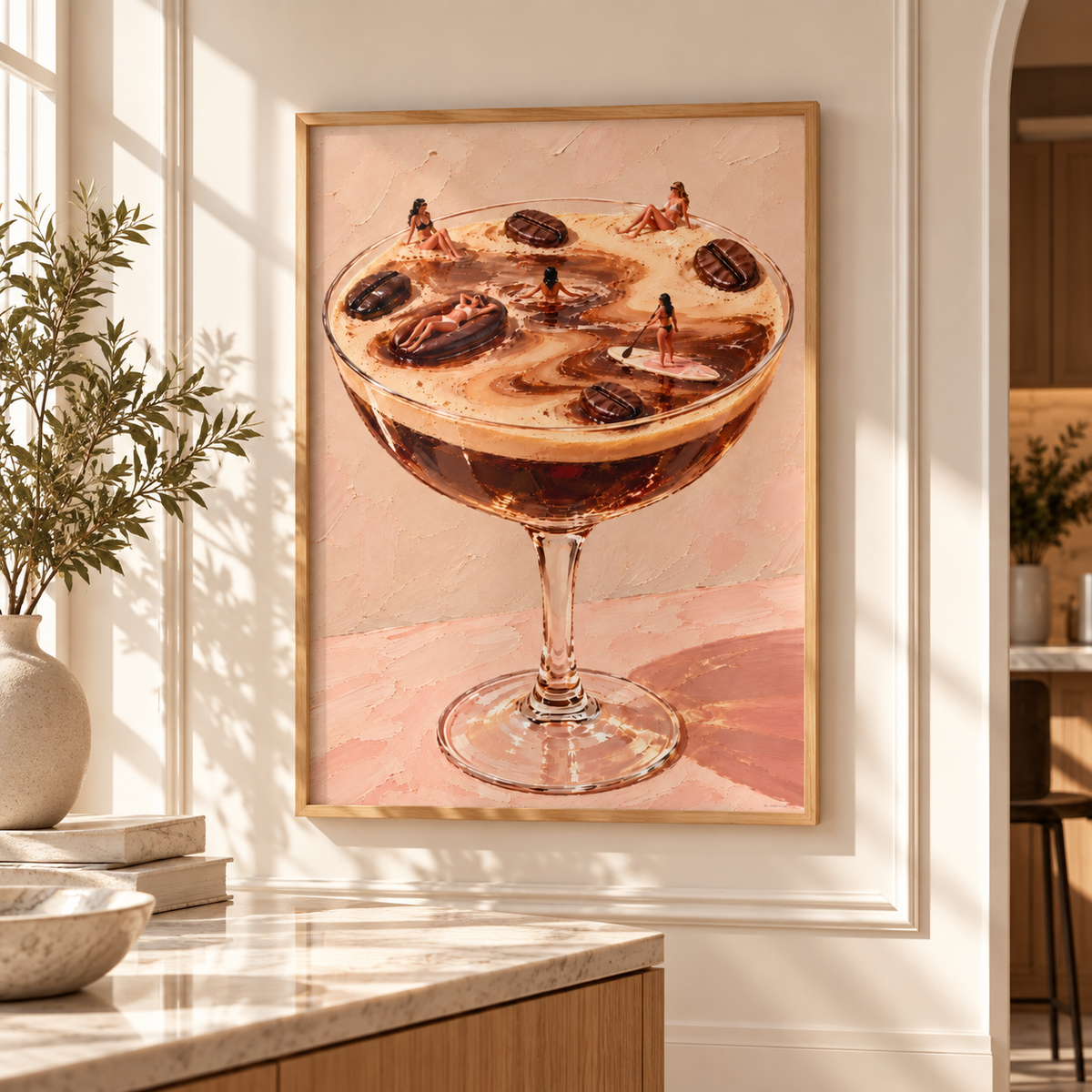 A framed art print depicting a cocktail in a coupe glass with coffee beans on top, hanging on a white wall in a bright, modern kitchen setting.