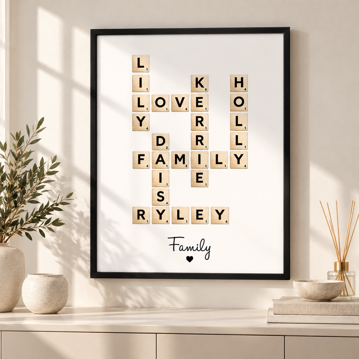 A framed personalized Scrabble-style letter tile print hangs on a beige wall above a console table. The letters form the words 'LOVE FAMILY RYLEY' with 'Family' and a small heart written below.