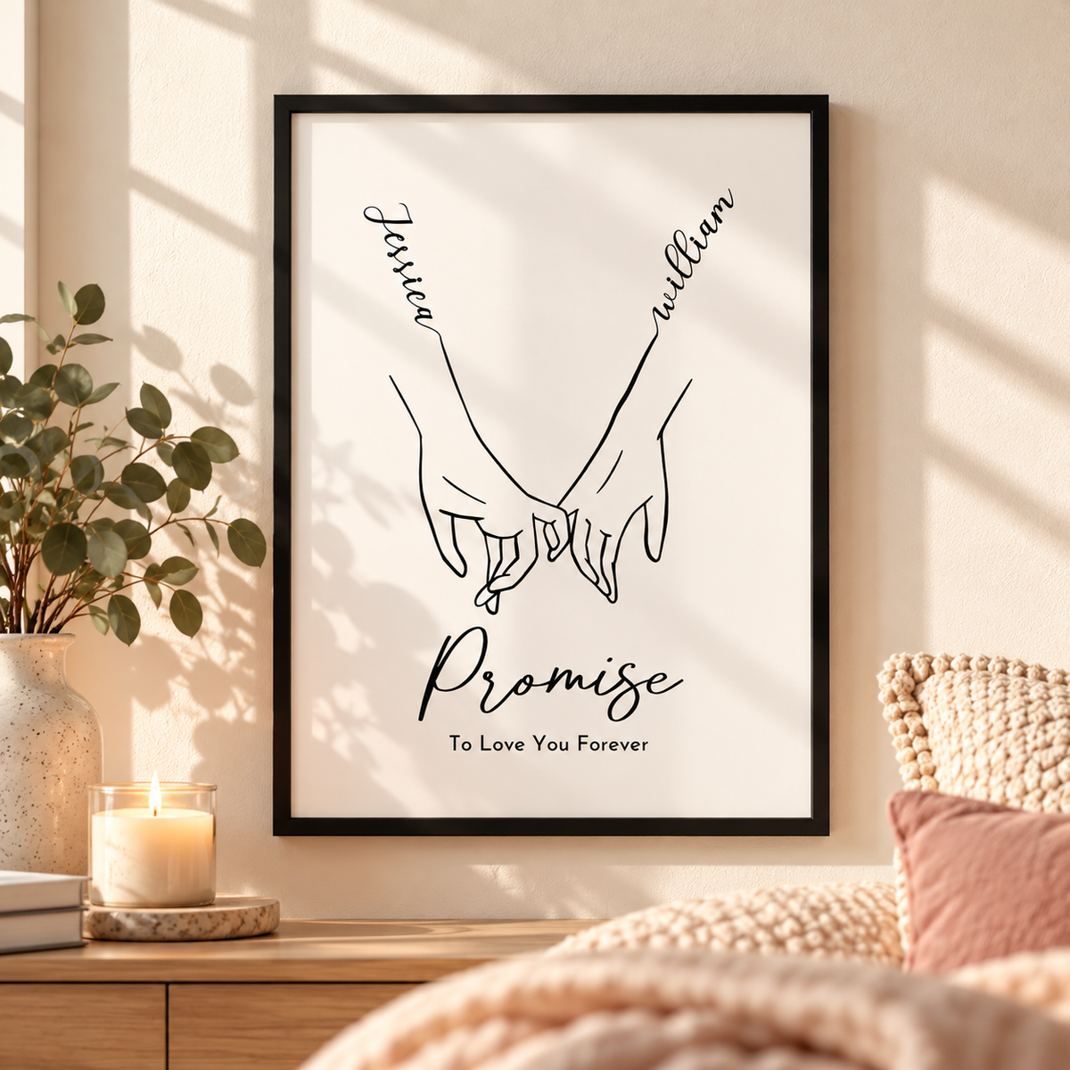 A framed minimalist art print hanging on a warm beige wall in a cozy bedroom setting. The print features a black line drawing of two hands holding, with the names 'Jessica' and 'William' above and the words 'Promise To Love You Forever' below.