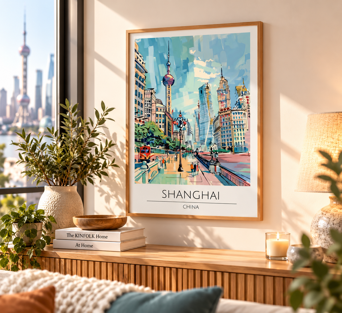A framed art print of a colorful Shanghai cityscape hangs on a warm beige wall in a beautifully styled room with a window view, plants, a lamp, and a wooden console table.